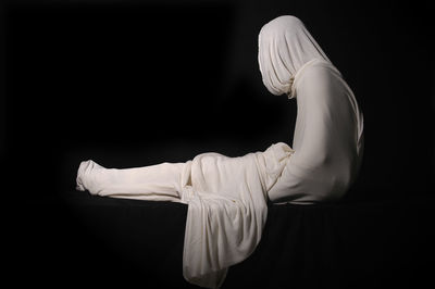 Person wrapped in white fabric against black background