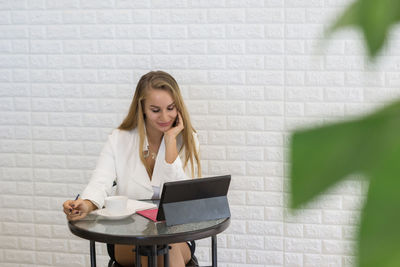 Young businesswoman using digital tablet while sitting at table in office