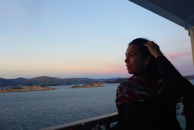 Woman looking away while standing by railing against sky during sunset