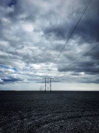 Low angle view of electricity pylons against clouds