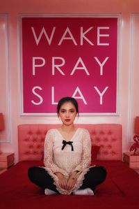 Portrait of a young attractive woman sit against wake pray slay quotes on the wall