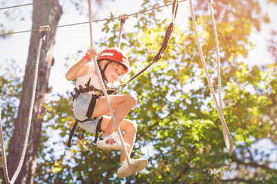 Low angle view of boy on rope against trees