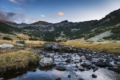 Stream flowing through rocks against sky