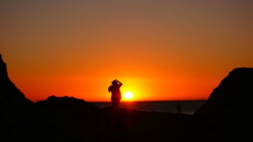 Silhouette man standing by sea against orange sky