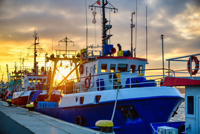 Boats moored at harbor against sky during sunset