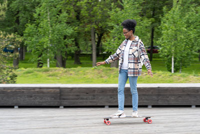 Skateboarding and urban lifestyle. trendy casual young african female on longboard in city park