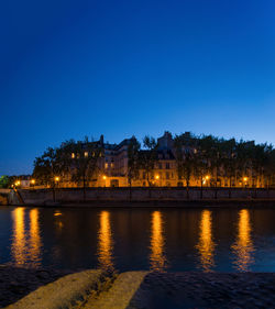 River by illuminated buildings against clear blue sky at night