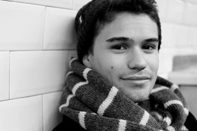 Close-up portrait of young man wearing scarf leaning on tiled wall