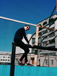 Full length of young woman balancing on railing against clear blue sky in city