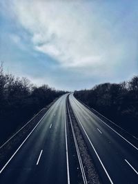 Empty road along plants and trees against sky