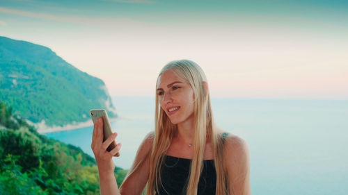 Portrait of smiling young woman looking at sea against sky