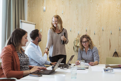 Smiling businesswoman shaking hand with businessman while female colleagues working at conference table