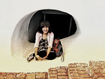 Portrait of young woman sitting against wall