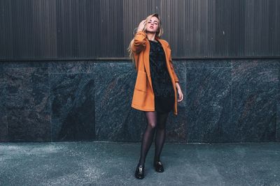 Portrait of young woman standing against wall