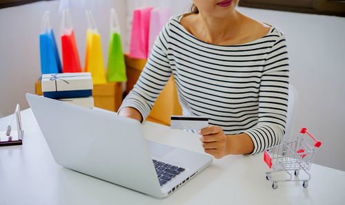 Midsection of businesswoman holding credit card while using laptop on table
