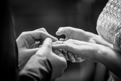 Cropped image of bridegroom putting ring in finger of bride