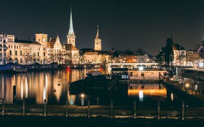 Illuminated buildings by river in city at night