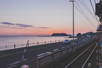 Railroad tracks and road by sea against sky during sunset