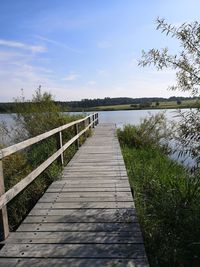 Boardwalk leading towards lake against sky