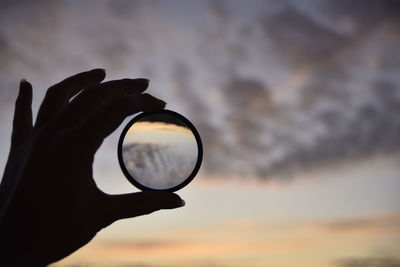 Silhouette person holding camera against sky during sunset