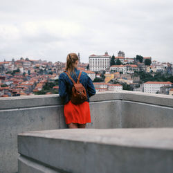 Rear view of woman on retaining wall against cityscape