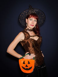 Portrait of woman with jack o lantern standing against black background