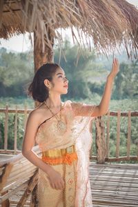 Girl in traditional clothing standing by thatched roof