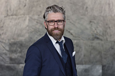 Portrait of smiling businessman in suit standing against wall