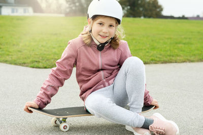Portrait of smiling girl sitting on skateboard at park
