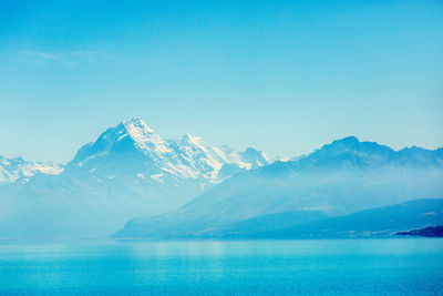 Scenic view of sea and snowcapped mountains against blue sky