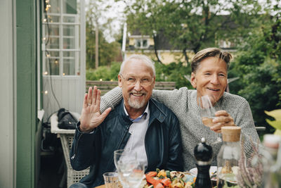 Happy male friends sitting at dining table enjoying dinner party in back yard