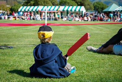 Rear view of boy with cricket bat sitting on playing field