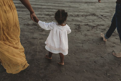 Young girl and mom walking away at beach holding hands