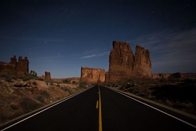 Road leading towards rock formation against sky at night