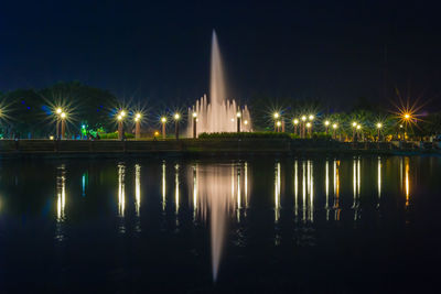 Illuminated street lights by lake against sky at night