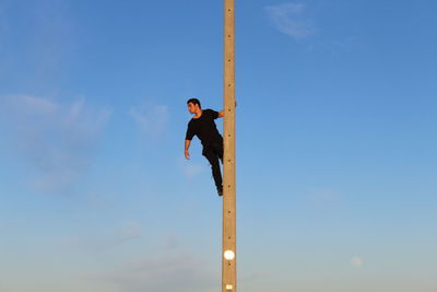 Low angle view of man on pole against blue sky