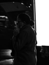 Side view of man holding mobile phone while standing in bus