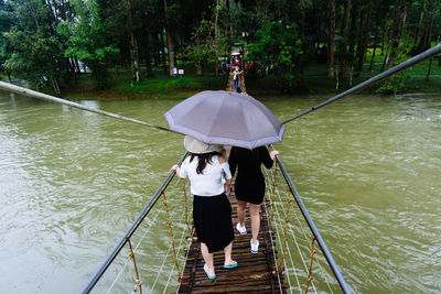 Rear view of woman holding umbrella by river