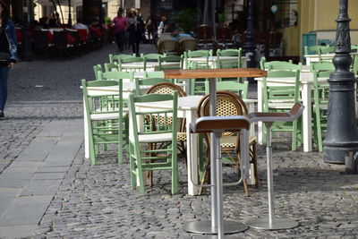 Empty chairs and tables at sidewalk cafe in city