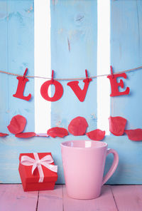 Close-up of love text hanging over petals and mugs