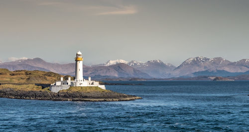 Eilean musdile lighthouse in scotland by sea and mountain against warm evening sky