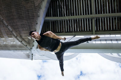 Low angle of fit male gymnast hanging on aerial straps during training in park