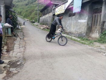 Man riding bicycle on road amidst buildings in city