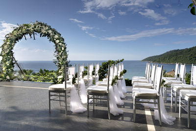 Empty chairs and table by sea against sky