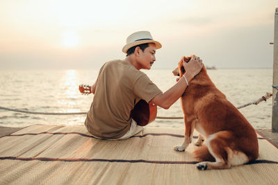 Man with dog sitting on shore against sea