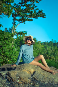 Young woman sitting on rock against trees