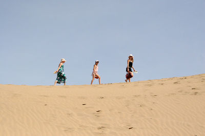 Low angle view of family walking at beach against clear sky
