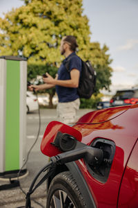 Electric cord charging car with man standing in background at station