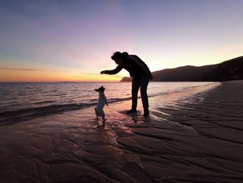 Silhouette woman on beach against sky during sunset