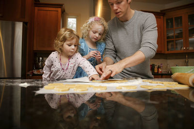 Father with daughters making cookies at table in kitchen